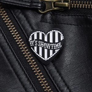 Close-up of black and white striped heart enamel pin with It's Showtime text on leather