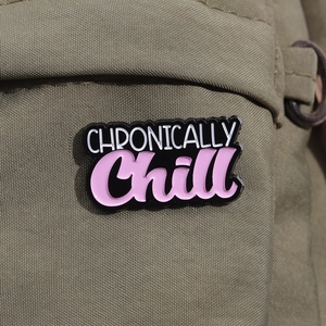 Detailansicht der 'CHRONICALLY Chill' Emaille-Anstecknadel auf grünem Canvas-Stoff