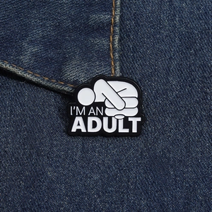 Gros plan détaillé du pin's émaillé I'M AN ADULT sur un fond de tissu en jean bleu foncé