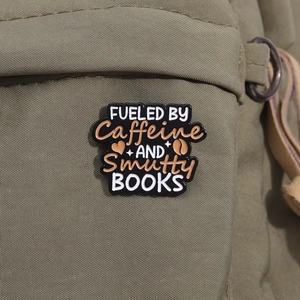 Detail of Fueled by Caffeine and Smutty Books enamel pin on a green canvas bag