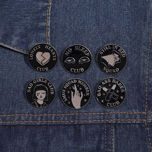 Close-up of six creative black enamel pins with slogans on denim fabric background