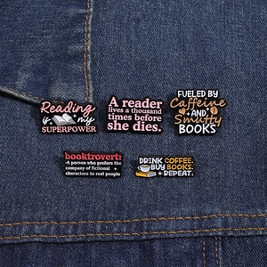 Macro detail of five enamel coffee and book pins pinned on blue denim fabric texture
