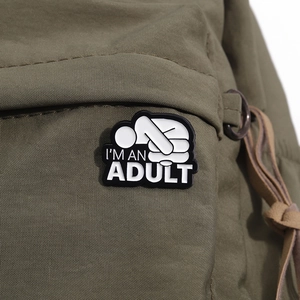 Gros plan du pin's émaillé I'M AN ADULT sur la sangle d'un sac à dos vert