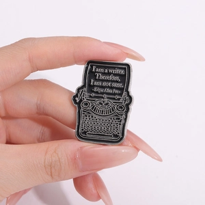 Detail of typewriter enamel pin with Edgar Allan Poe quote held in hand for scale