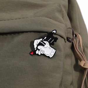Detail of cartoon tattoo machine enamel pin with red heart on olive green canvas bag