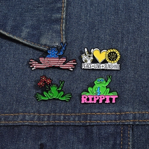 Set of four unique enamel pins featuring cartoon frogs and sunflowers on denim fabric