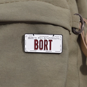 Macro shot of Bort license plate enamel pin attached to a green canvas backpack