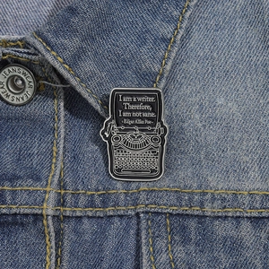 Detail of typewriter enamel pin with Edgar Allan Poe quote on a denim jacket collar