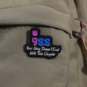 Detail of metal enamel pin with 988 crisis hotline and inspirational quote on canvas