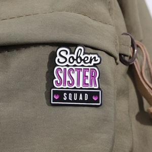 Detail of Sober SISTER SQUAD enamel pin with purple hearts on green canvas fabric