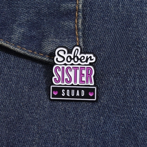 Close-up of Sober Sister Squad enamel pin with purple hearts on blue denim fabric