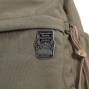 Detail of a vintage typewriter enamel pin with Edgar Allan Poe quote on a green backpack