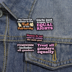 Lot de cinq broches en émail aux slogans féministes fixées sur un col en jean bleu
