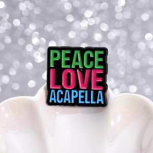 Detail van zwarte emaille speld met kleurrijke Peace Love Acapella letters op een tray