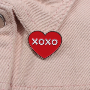 Vue macro d'une broche XOXO en émail rouge en forme de cœur sur tissu denim rose