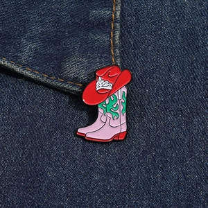 Gros plan du pin's émaillé botte de cowboy rose et chapeau rouge sur denim bleu
