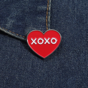 Gros plan d'un badge en émail cœur rouge XOXO épinglé sur un tissu en jean bleu foncé