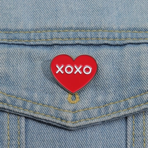 Détail d'un pin's émaillé en forme de cœur rouge XOXO sur un tissu en jean bleu