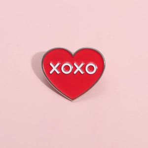 Broche en émail cœur rouge avec lettrage XOXO blanc et bordure argentée sur fond rose
