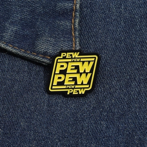 Detail of a Pew Pew enamel pin with yellow text on blue denim fabric background