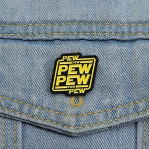 Macro detail of black and yellow Pew Pew enamel pin on light blue denim jacket