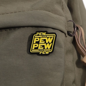 Macro shot of yellow and black PEW PEW enamel pin attached to green canvas fabric
