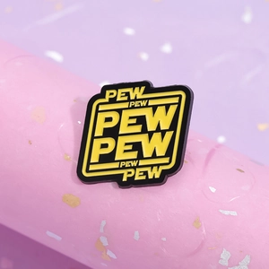 Macro shot of Pew Pew enamel pin badge with yellow sci-fi lettering on black metal