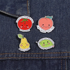 Close-up of four colorful enamel fruit pins with puns on dark blue denim fabric