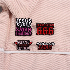 Close-up of four black punk enamel pins with red gothic text on pink denim fabric