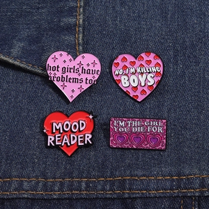 Set of four trendy enamel pins with pink heart motifs and slogans on denim background