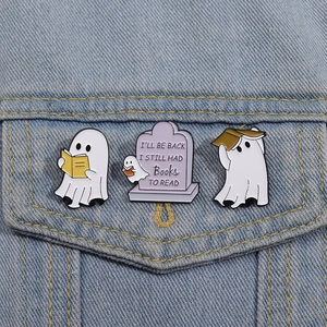 Close-up of three ghost reading enamel pins pinned on a denim jacket pocket fabric