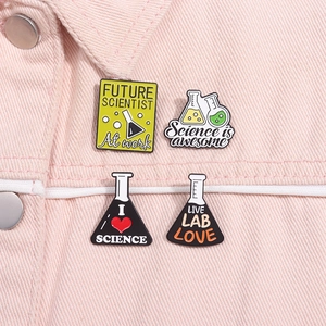 Dettaglio di quattro spille smaltate a tema scientifico su tessuto denim rosa