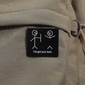Detail of square black enamel pin with I've got your back quote on green canvas bag
