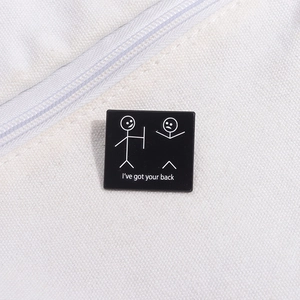 Close-up of a black square metal pin with stick figure drawing and 'I've got your back' text