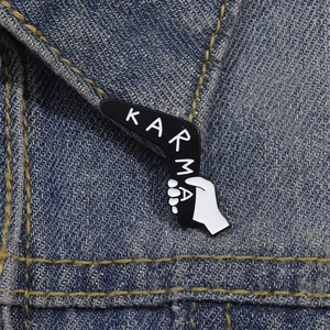 Broche émaillée boomerang Karma noir et blanc portée sur une veste en jean bleu