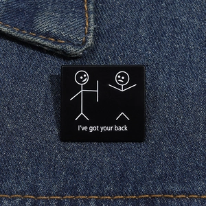 Detailed view of square enamel pin with I've got your back illustration on denim jacket