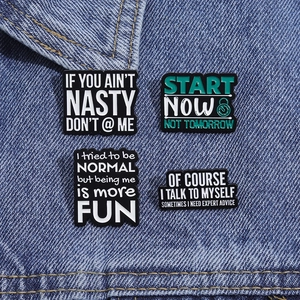 Detail view of four enamel quote pins including Start Now Not Tomorrow on denim fabric