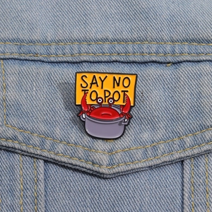 Détail d'un pin's en émail crabe rigolo sur une veste en jean bleue en coton