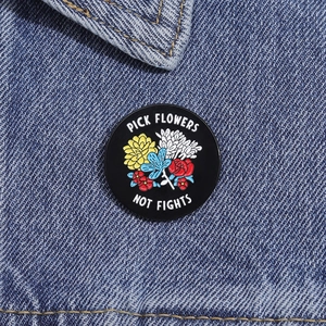 Detailed close-up of a Pick Flowers Not Fights enamel pin on blue denim fabric