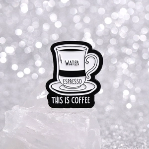 Cartoon enamel coffee cup brooch with 'THIS IS COFFEE' text in black and white