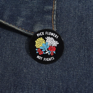 Macro shot of circular black enamel pin with colorful floral motif on blue denim fabric