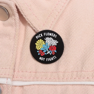 Detail of round enamel pin with floral design and Pick Flowers Not Fights quote