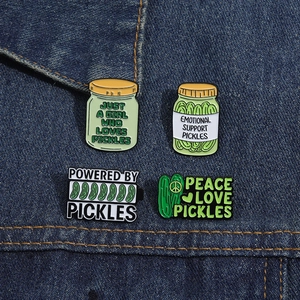 Set of four green pickle enamel pins pinned on denim showing various humorous text designs