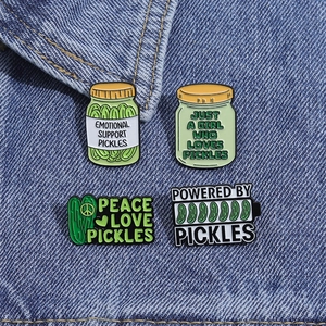 Set of four green pickle enamel pins attached to blue denim fabric showing detailed texture
