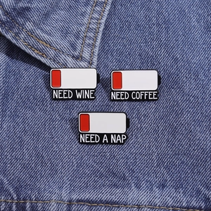 Detail of battery pins NEED WINE, NEED COFFEE and NEED A NAP on blue denim fabric