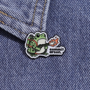 Détail du pin's en émail grenouille avec texte commit arson sur tissu en jean