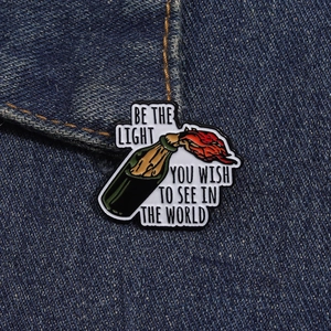 Detail of enamel molotov cocktail brooch with motivational text on denim fabric background