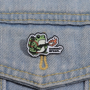 Détail d'un pin's en émail de grenouille rigolote avec un lance-flammes sur denim