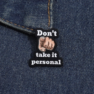 Macro shot of an enamel pin on denim showing the text Don't take it personal