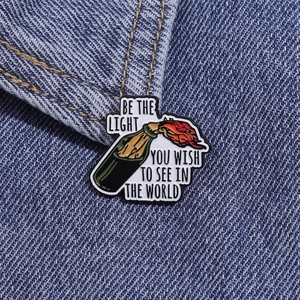 Detail view of enamel Molotov cocktail pin with motivational quote on denim background